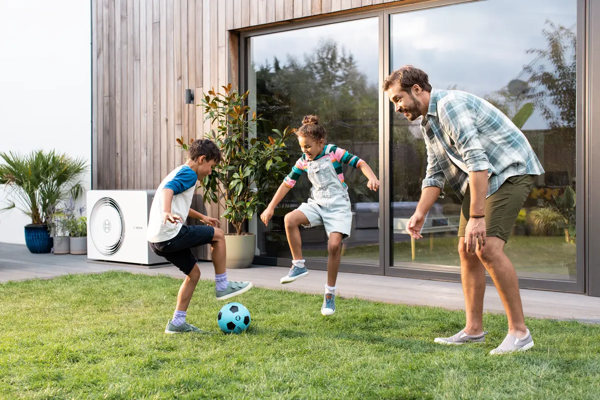 Bosch Compress 5800i AW am Wohnhaus neben einer Familie im Garten – Herstellermotiv